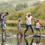 Family Crossing River Whilst Hiking In UK Lake District